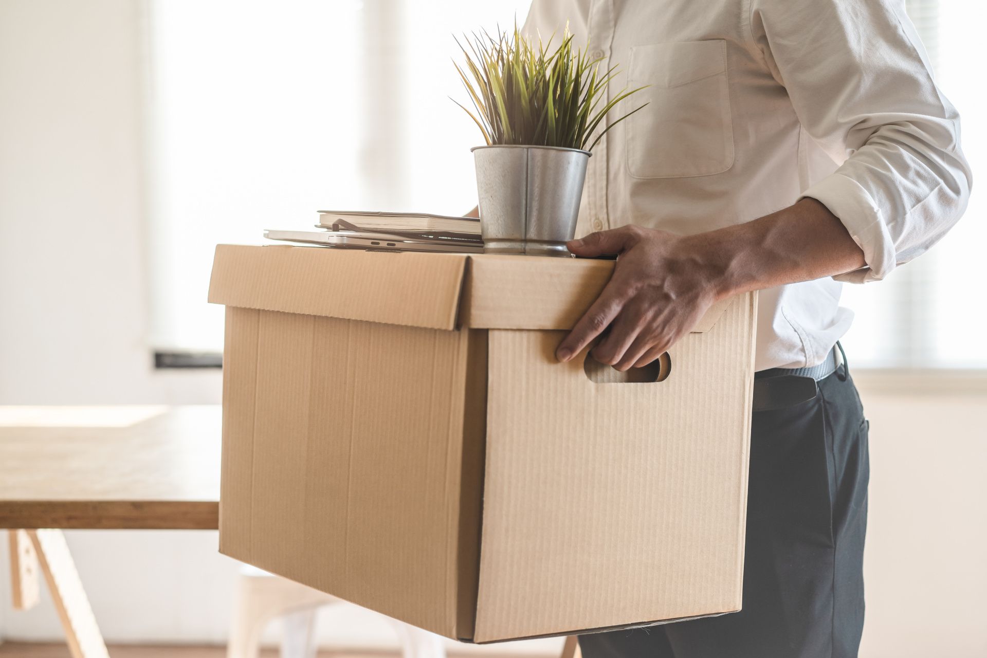 person carrying box and belongings out of office to downsize